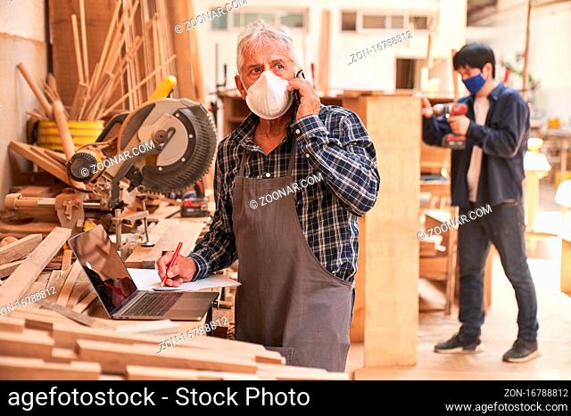 Handwerker mit Maske wegen Covid-19 mit Handy bei Kundengespräch in Schreinerei