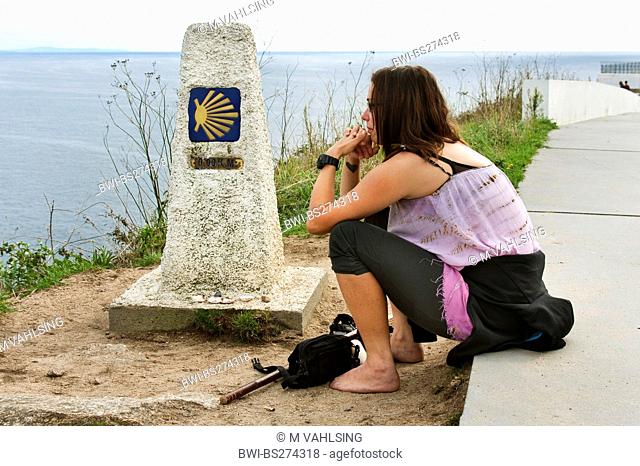young woman at kilometre stone zero reflecting her pilgrimage, Spain, Galicien, Provinz A Coruña, A Corua, Kap Finisterre, kelt. Fisterra