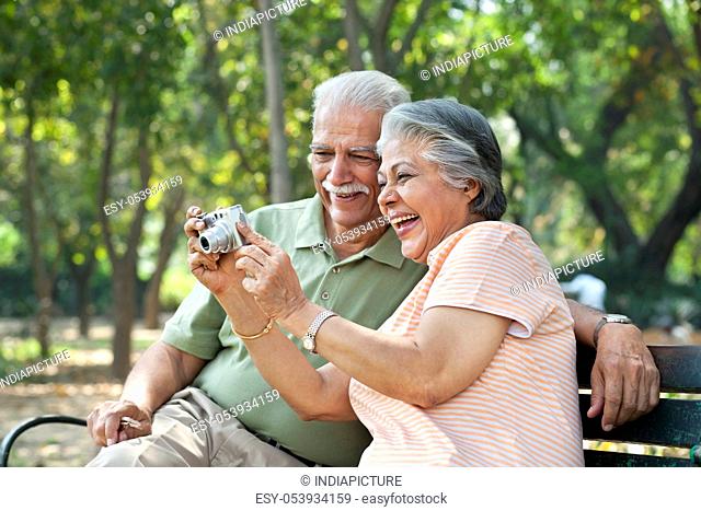 Cheerful couple using digital camera at park