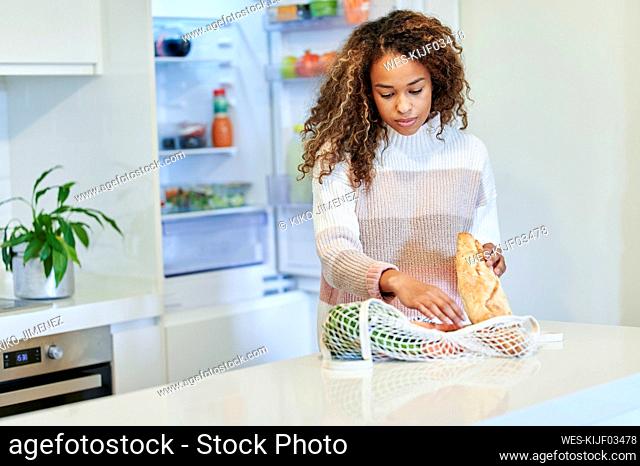 Afro young woman organizing groceries in kitchen at home
