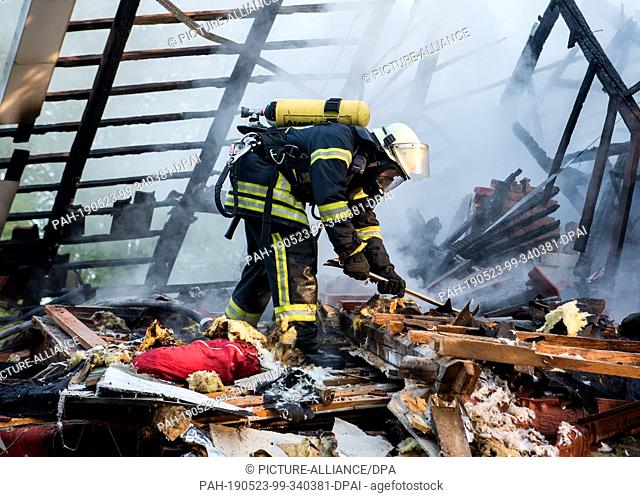 23 May 2019, Schleswig-Holstein, Wohltorf: A firefighter pulls apart debris from a house that was destroyed in a fire. The fire department was still looking for...