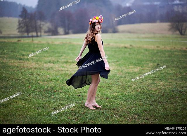 Young woman with wreath of flowers is dancing on a meadow