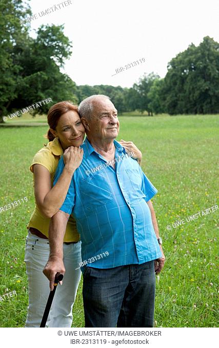 Woman hugging an elderly man with a walking cane in a meadow