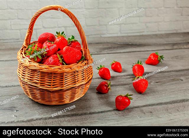Basket with strawberries, some of them spilled on gray wood desk