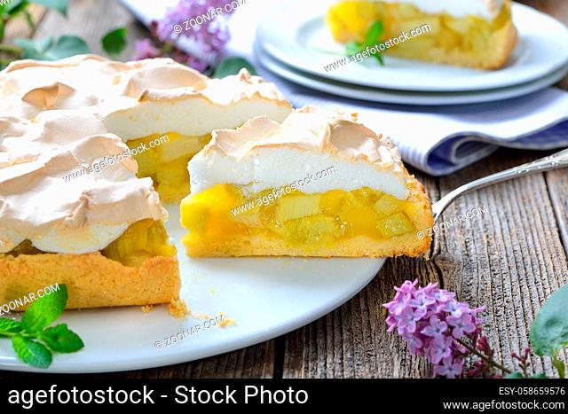 Leckerer Rhabarberkuchen mit Baiserhaube auf einem Holztisch mit frühlingshafter Fliederdeko - Delicious rhubarb cake with springlike lilac decoration
