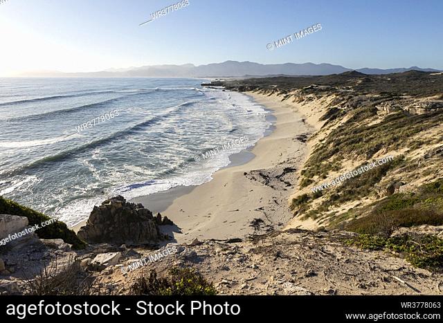 Elevated view from cliffs above a sandy beach, waves breaking on shore and view along the coast