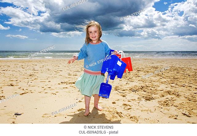 Young girl holding bucket and spade on beach, Walberswick, Suffolk, England, UK