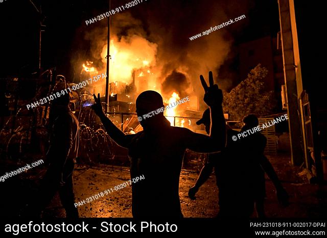 18 October 2023, Lebanon, Beirut: A Lebanese protester flashes the victory sign in front of a burning building just outside the US Embassy during a protest in...
