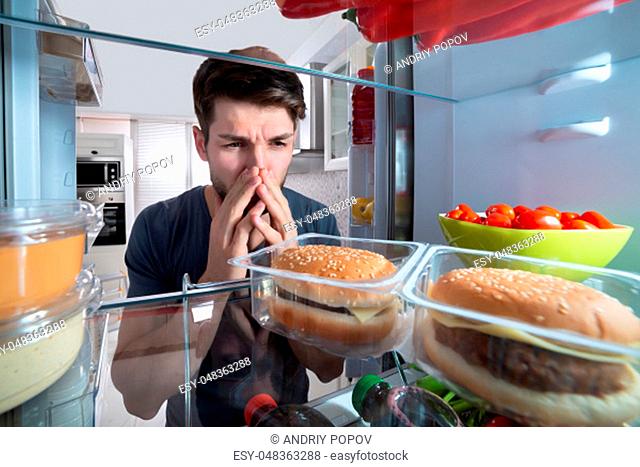 Young Man Holding His Nose After Recognizing Bad Smell Coming Out From The Refrigerator