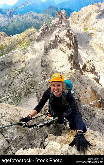 Vertical view of an attractive female climber on a steep Via Ferrata in the Italian Dolomites with a great view behind