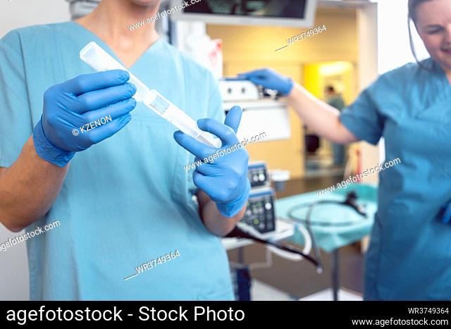 Nurse preparing anesthetic for surgery in hospital, patient and second nurse in the background