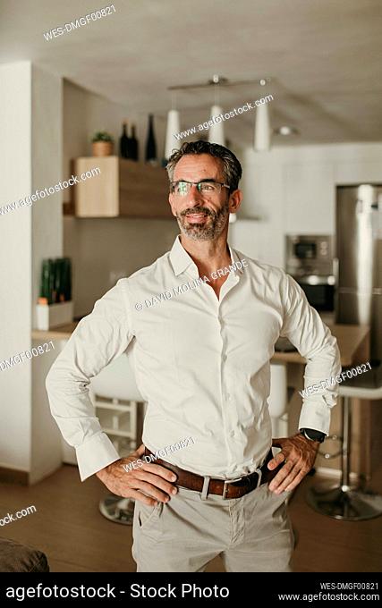 Confident mature businessman with arms akimbo at home