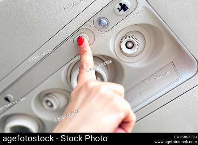 Woman hand up to adjust console panel at the air conditioner above the seat in cabin of low cost commercial airplane