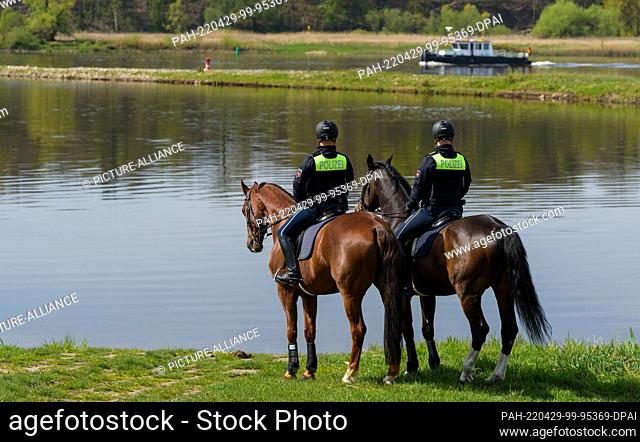 29 April 2022, Lower Saxony, Herrenhof: The police officers, Michael Reh (l) on Filou and Tjaard Kirschtowski on Herkules stand on the banks of the Elbe during...
