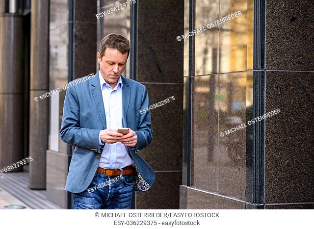 A middle age businessman walking next to the office building while using his smartphone