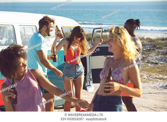Front view of happy group of diverse friends dancing together near camper van at beach