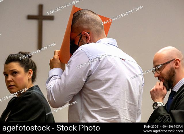 14 June 2023, Bavaria, Munich: The defendant covers his face with a file cover in the courtroom. On the left is his lawyer Francesca Rossiello-Bianco