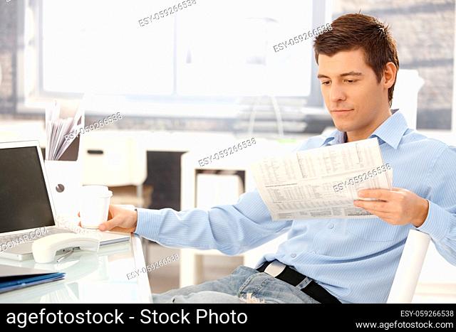 Businessman taking break in office, reading newspaper, having coffee, putting phone aside