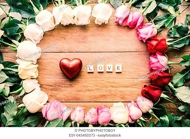 Colorful roses lined up on a wooden floor with heart and word ""LOVE"" - concept for love