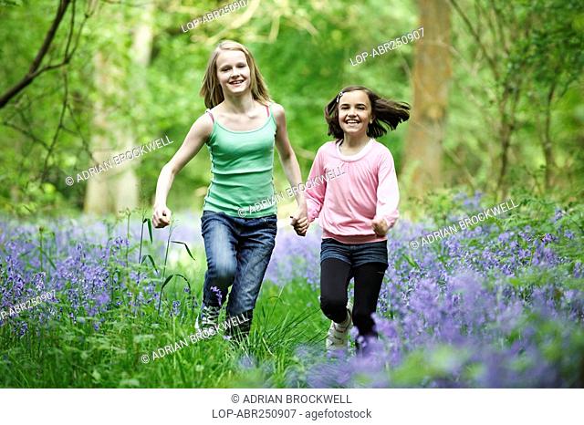 England, Buckinghamshire, Stokenchurch, Two young girls running hand in hand through a wood full of Bluebells