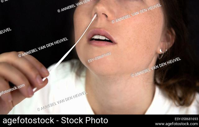 Young woman taking a Covid-19 SARS-CoV-2 test during Corona pandemic on dark black background, quick home test coronavirus closeup nose swab