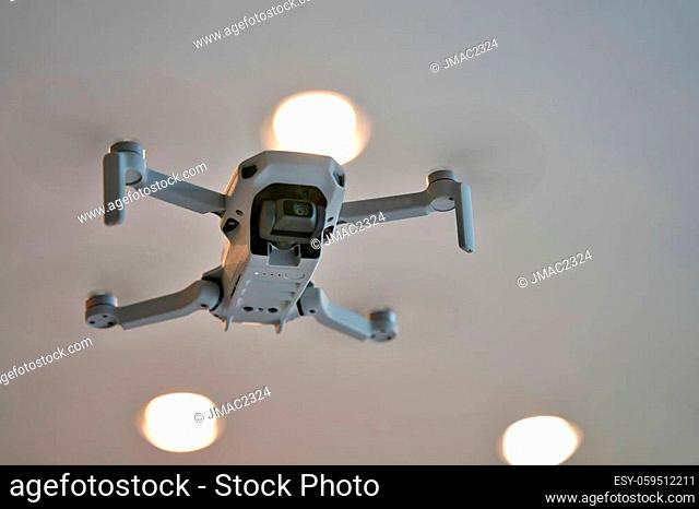 Drone flying indoors with ceiling visible in background. Underside of drone in flight inside of house