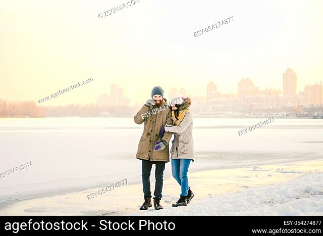 Theme Christmas holidays winter new year. Young stylish Caucasian loving couple Heteresexual walking on the shore of a frozen lake. Date
