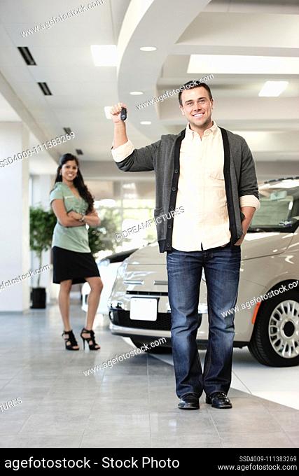 Proud man holding keys to new car in showroom