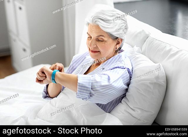 happy old woman with health tracker sitting in bed