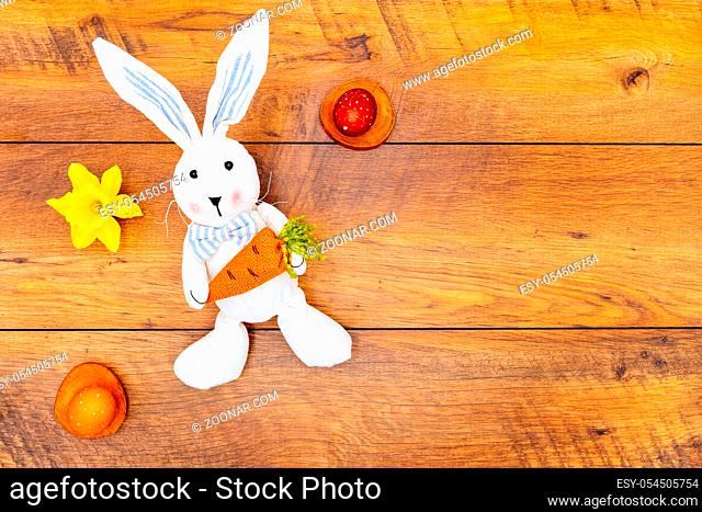 Colourful wax painted Easter eggs in pastel colours on wooden pads, daffodil and Easter bunny with carrot on vintage reclaimed oak background top view