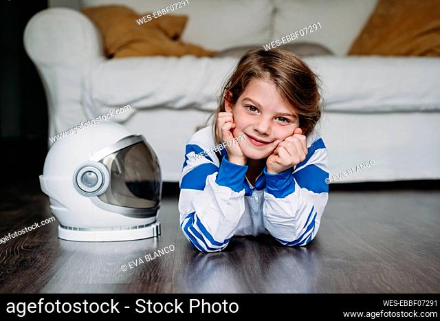 Smiling girl wearing space costume lying by helmet on floor in living room