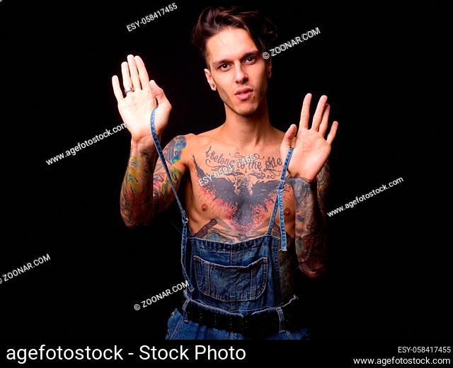 Studio shot of young handsome rebellious man shirtless against black background