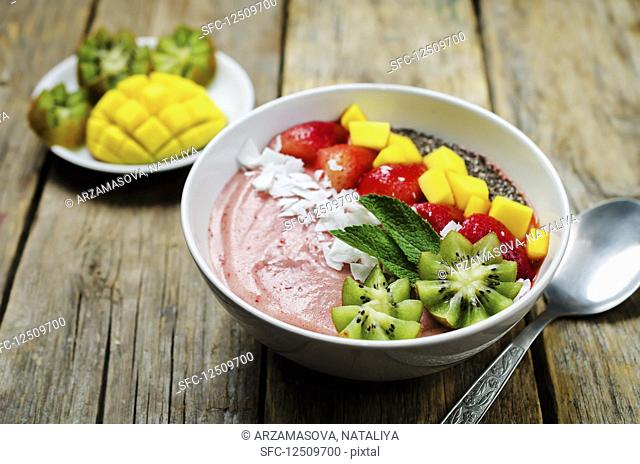 A breakfast bowl with strawberry smoothie, kiwi, coconut flakes, strawberries, mango and chia seeds