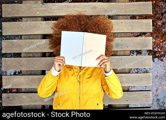 Woman covering face with book lying on bridge in autumn forest