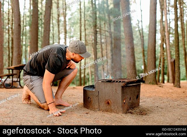 Canada, Yukon, Whitehorse, Man making fire on fire pit in campsite