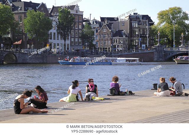 People relaxing by River Amstel Amsterdam Holland