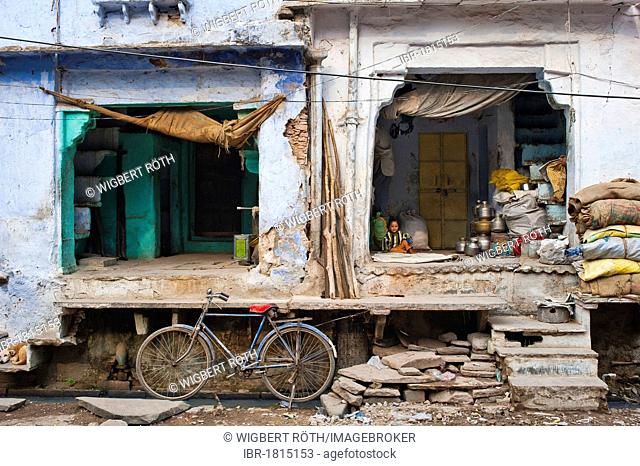 Old bicycle in front of a shop in an alleyway, little child playing on a blanket at back, Bundi, Rajasthan, India, Asia
