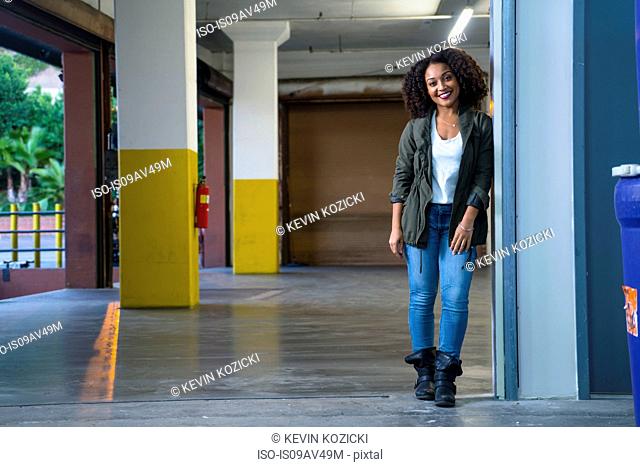 Mid adult woman in lobby leaning against wall looking at camera smiling