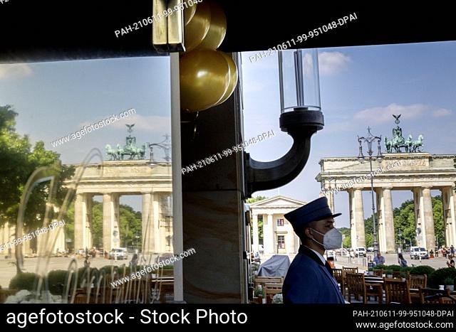 11 June 2021, Berlin: A bellboy stands under gold-coloured balloons in front of the hotel entrance of the Hotel Adlon Kempinski at Pariser Platz near the...