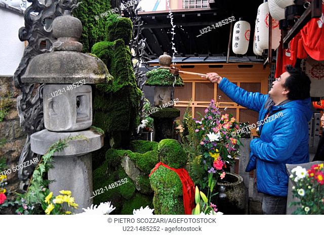Osaka (Japan): a believer throwing water to the moss-covered statue of Fudo-myoo at the Hozen-ji temple in Dotombori