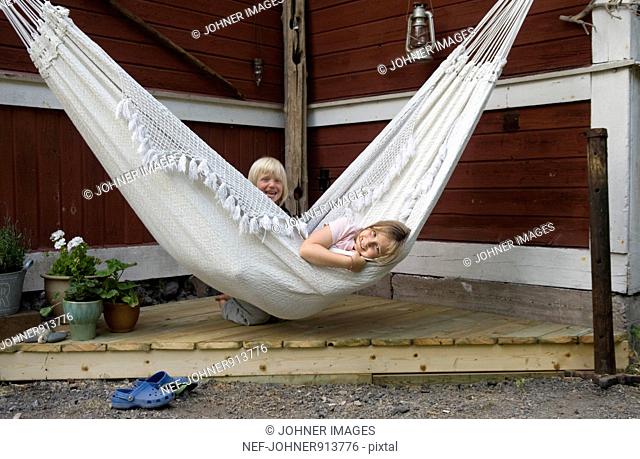 Girl relaxing in hammock, boy in background