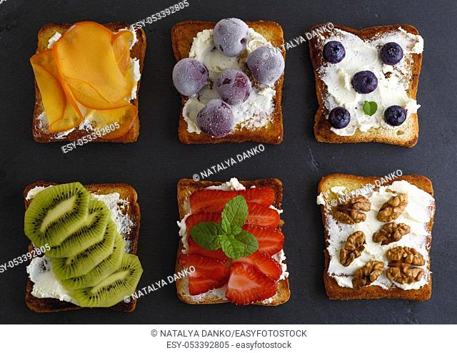 French toast with cottage cheese, strawberries, kiwi and blueberries, walnuts, cherries, persimmons on a black board, top view