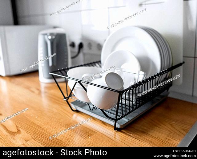 Budget and lightweight antimicrobial dish drainer with drain board at modern scandinavian kitchen. Dish rack holds many dishes and cups against wooden...