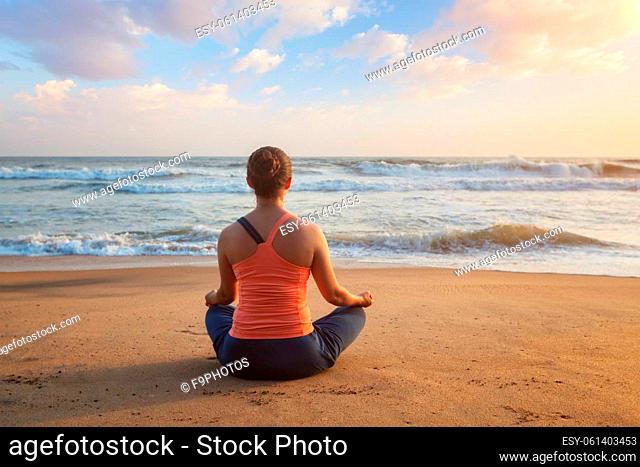 Woman doing yoga - meditating and relaxing in Padmasana Lotus Pose outdoors at tropical beach on sunset