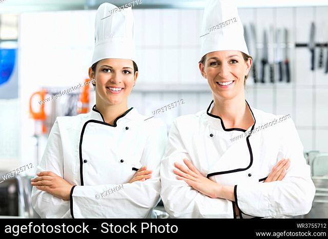 Female chefs wearing typical working clothes standing behind the stove in canteen
