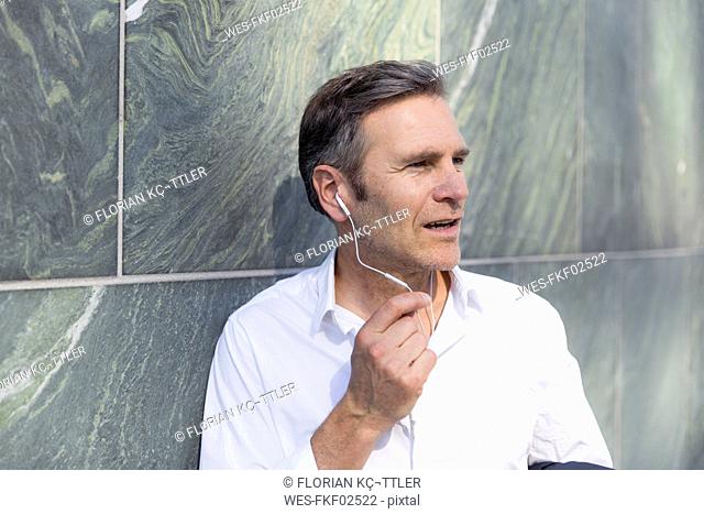Mature businessman with earphones at a wall