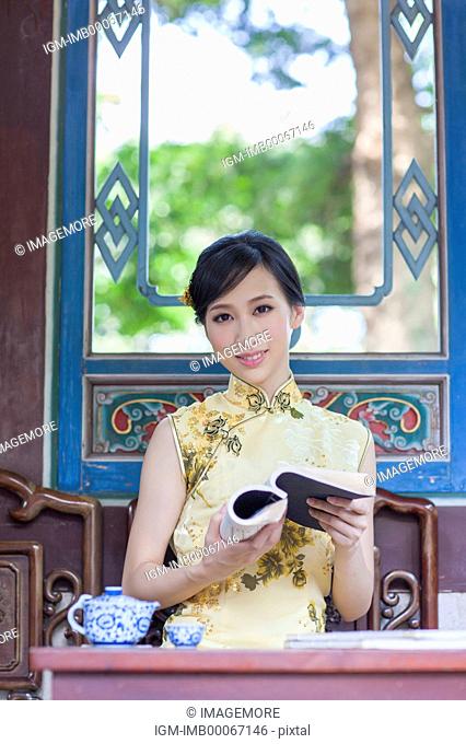 Young woman with cheongsam holding a book and smiling at the camera