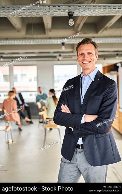 Mature male entrepreneur standing with colleagues in background at office