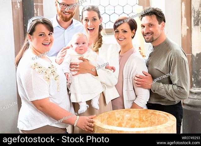 Parents and godparents stand at the baptismal font with the baby in a church