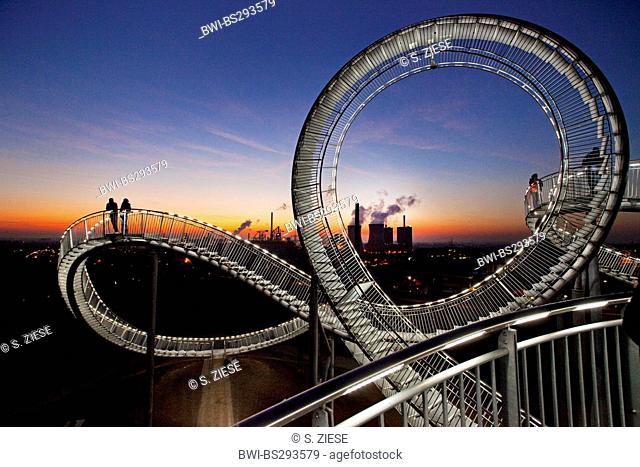 persons on the illuminated landmark Tiger and Turtle on stockpile Angerpark in front of the cooling towers steel work Krupp Mannesmann in the evening, Germany